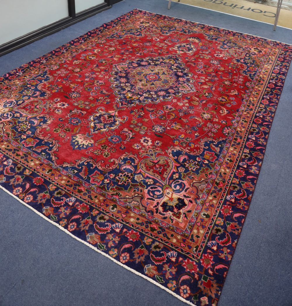 A Mashaed Khorason rug with central medallion and trailing foliate design on a red field, wide border with guard stripes, 355cm x 255cm